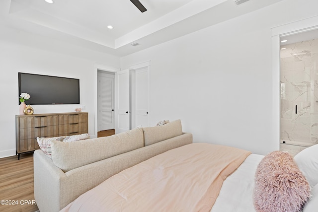 bedroom with a tray ceiling, hardwood / wood-style floors, ensuite bath, and ceiling fan