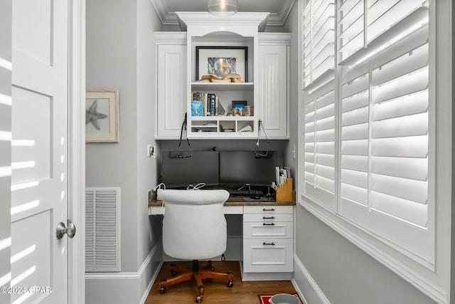 office space featuring baseboards, visible vents, built in desk, wood finished floors, and ornamental molding