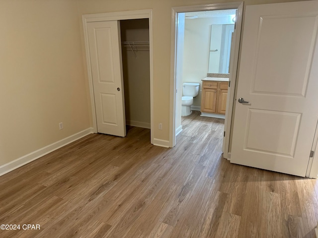 unfurnished bedroom featuring ensuite bath, light wood-type flooring, and a closet