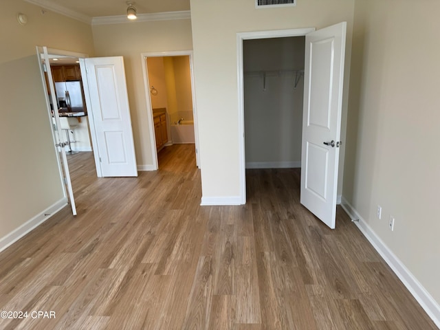 unfurnished bedroom with stainless steel fridge, crown molding, hardwood / wood-style flooring, a spacious closet, and a closet