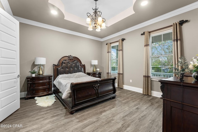 bedroom featuring a raised ceiling, light wood-type flooring, crown molding, and a chandelier