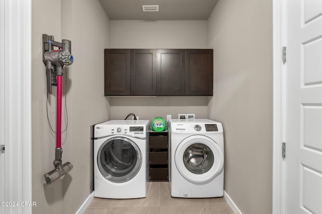 clothes washing area with washing machine and dryer, light tile patterned floors, and cabinets