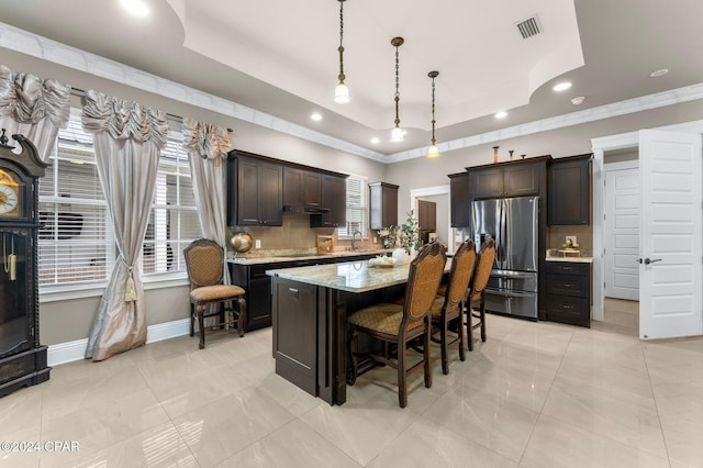 kitchen with stainless steel fridge, dark brown cabinets, a tray ceiling, a kitchen island, and hanging light fixtures