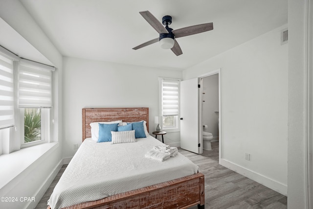 bedroom with multiple windows, ceiling fan, ensuite bath, and light wood-type flooring