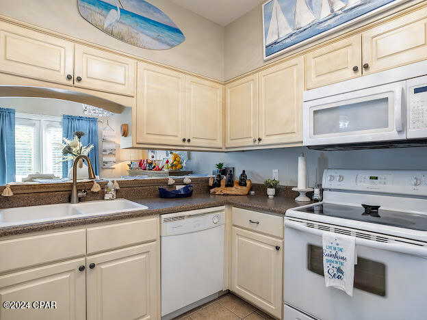 kitchen featuring cream cabinetry, light tile patterned floors, white appliances, and sink