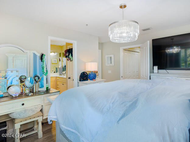 bedroom with ensuite bath, dark hardwood / wood-style flooring, and a notable chandelier