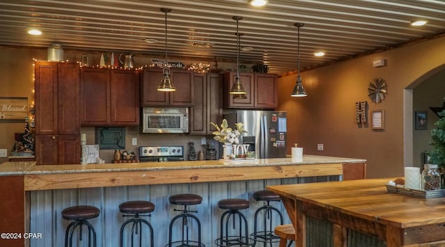 kitchen featuring stainless steel appliances, hanging light fixtures, light stone counters, and a center island