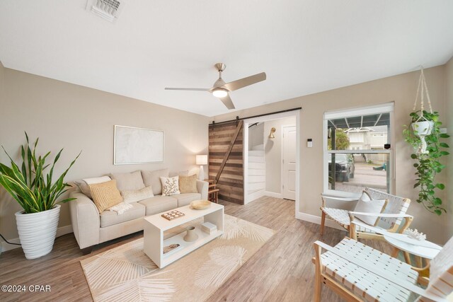 living room featuring a barn door, ceiling fan, and light hardwood / wood-style floors