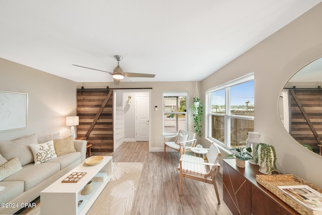 living area with light wood finished floors, a barn door, ceiling fan, baseboards, and stairs