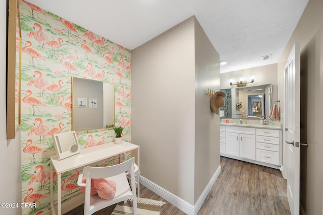 hallway featuring wallpapered walls, baseboards, a sink, and wood finished floors