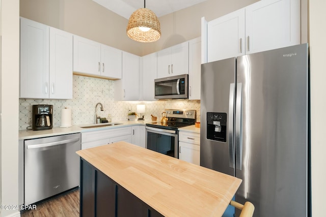 kitchen with stainless steel appliances, light countertops, hanging light fixtures, white cabinets, and a sink