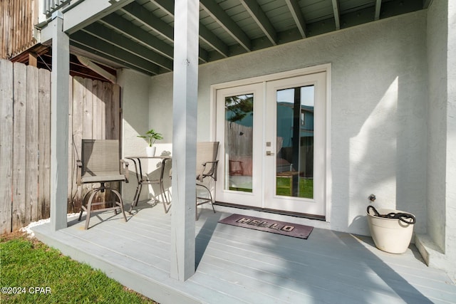 view of exterior entry featuring french doors, a wooden deck, and stucco siding