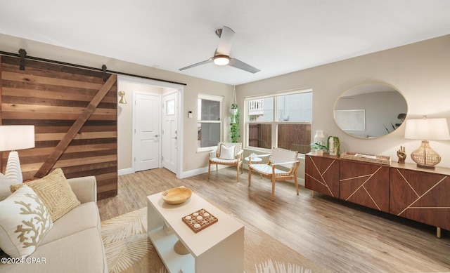 living room with baseboards, a barn door, a ceiling fan, and wood finished floors