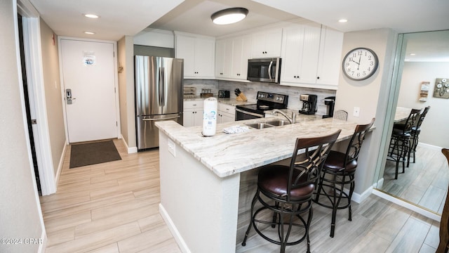 kitchen featuring a kitchen bar, kitchen peninsula, stainless steel appliances, light stone countertops, and white cabinets