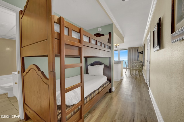 bedroom featuring crown molding, light hardwood / wood-style floors, ensuite bath, and an inviting chandelier