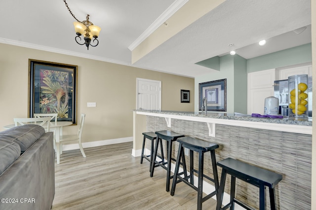 kitchen featuring light hardwood / wood-style floors, white cabinetry, a kitchen breakfast bar, a chandelier, and crown molding