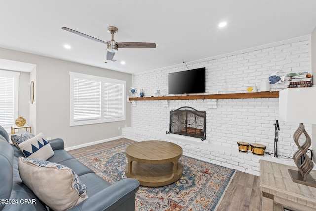 living room featuring dark wood-type flooring, a fireplace, ceiling fan, and brick wall