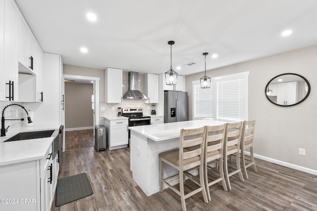 kitchen with wall chimney exhaust hood, sink, hanging light fixtures, appliances with stainless steel finishes, and white cabinets