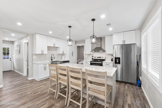 kitchen featuring white cabinets, decorative light fixtures, stainless steel appliances, and wall chimney exhaust hood