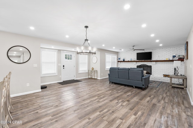 living room with a brick fireplace, ceiling fan with notable chandelier, hardwood / wood-style flooring, and brick wall