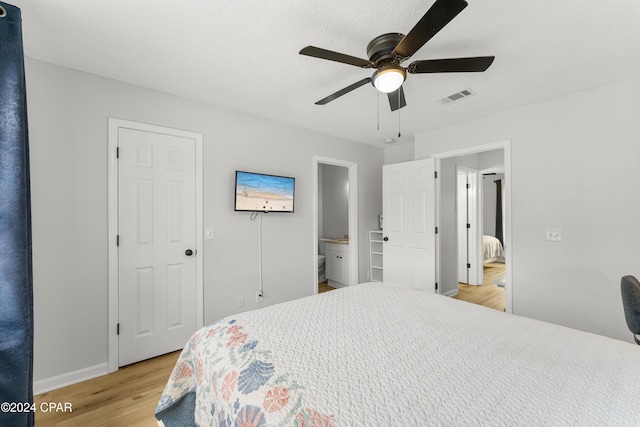 bedroom featuring light wood-type flooring, ceiling fan, a textured ceiling, and connected bathroom