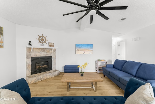 living room with hardwood / wood-style floors, a textured ceiling, a stone fireplace, lofted ceiling with beams, and ceiling fan