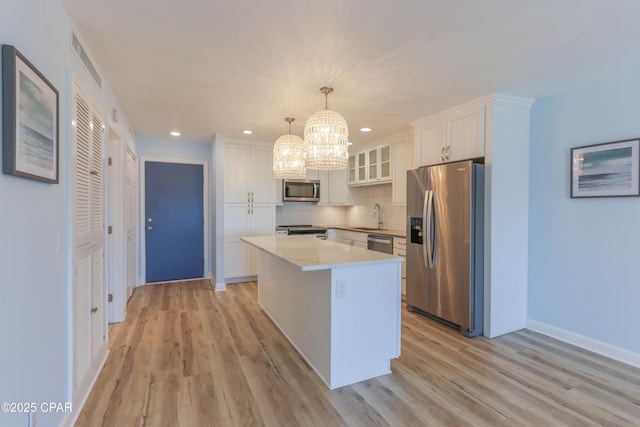 kitchen with stainless steel appliances, a kitchen island, a chandelier, and light wood finished floors