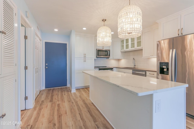 kitchen with a center island, a notable chandelier, white cabinets, stainless steel appliances, and a sink