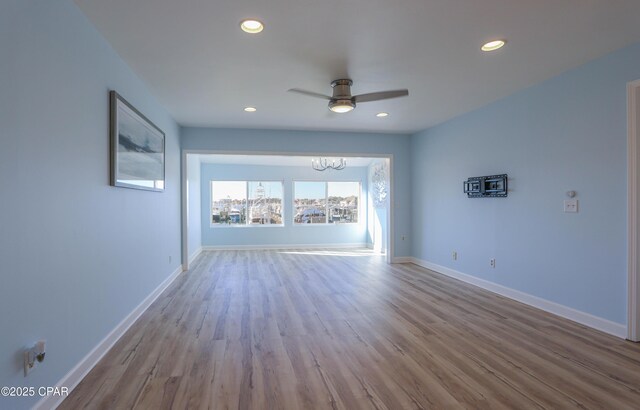 empty room with wood finished floors, ceiling fan with notable chandelier, and baseboards