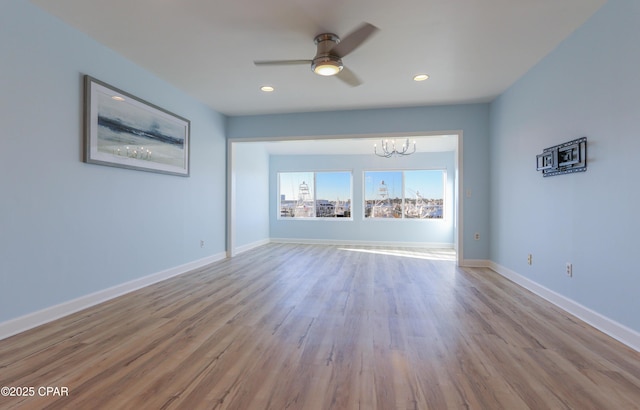 empty room with ceiling fan with notable chandelier, recessed lighting, wood finished floors, and baseboards