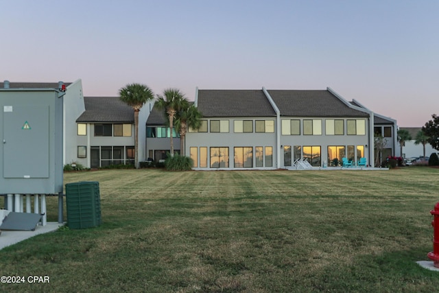 back of house at dusk featuring a yard