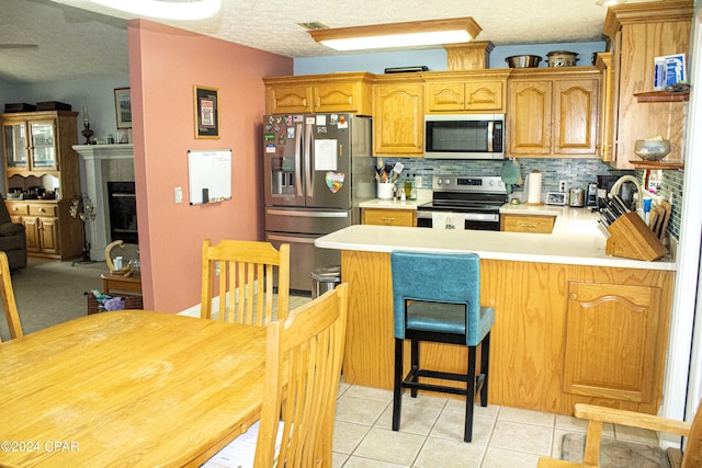 kitchen with decorative backsplash, kitchen peninsula, a breakfast bar, stainless steel appliances, and light tile patterned floors