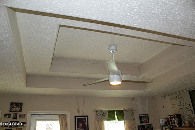 interior details featuring ceiling fan, a raised ceiling, and a textured ceiling