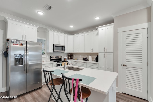 kitchen with appliances with stainless steel finishes, an island with sink, sink, white cabinets, and a kitchen breakfast bar