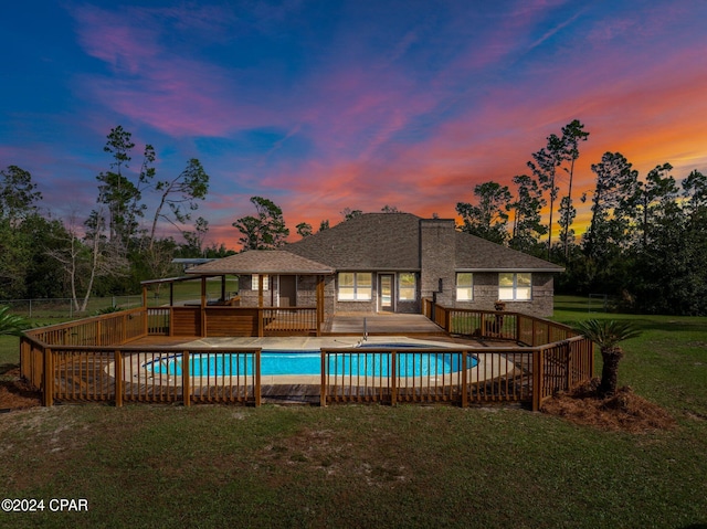 pool at dusk featuring a patio and a lawn