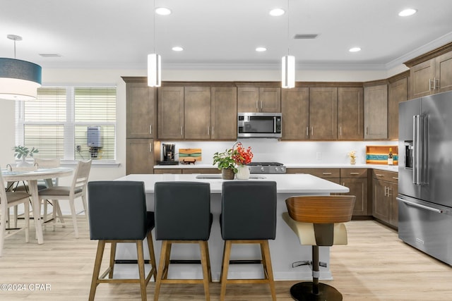 kitchen with appliances with stainless steel finishes, hanging light fixtures, a center island, and crown molding