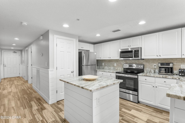 kitchen featuring white cabinets, stainless steel appliances, light hardwood / wood-style flooring, and light stone countertops