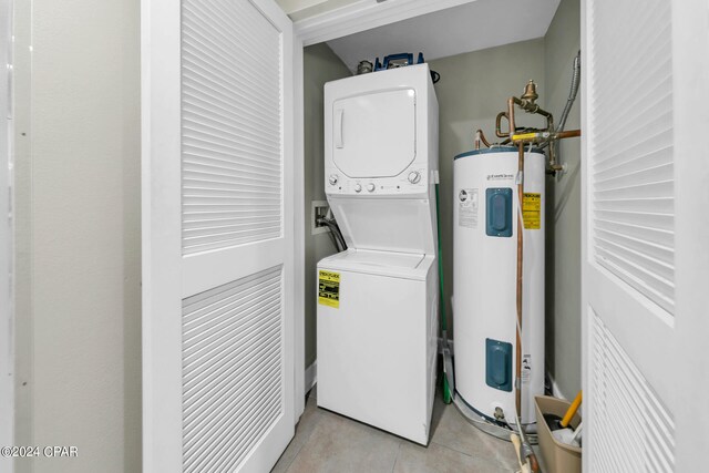 washroom with light tile patterned flooring, stacked washer / dryer, and water heater