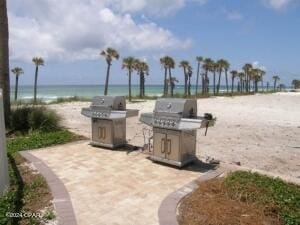 view of patio / terrace featuring a view of the beach, an outdoor kitchen, a water view, and a grill