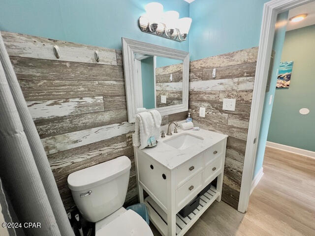 bathroom featuring an inviting chandelier, wood walls, toilet, vanity, and hardwood / wood-style flooring