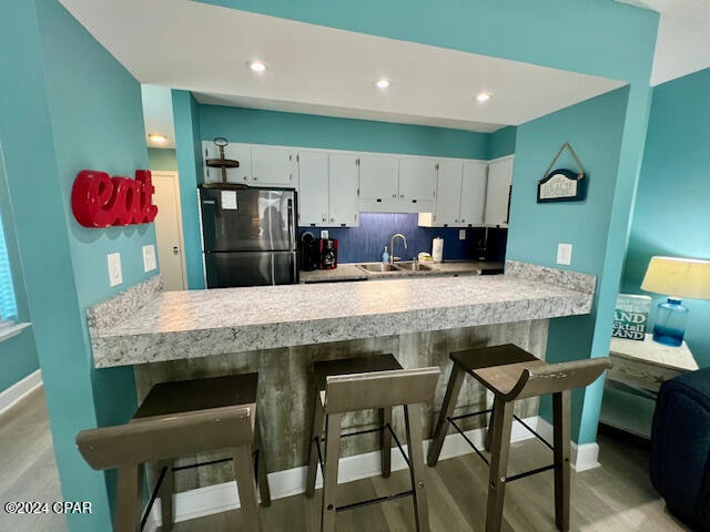 kitchen featuring backsplash, white cabinets, sink, light hardwood / wood-style flooring, and stainless steel fridge