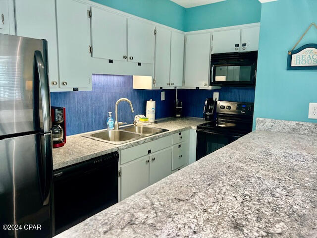 kitchen featuring backsplash, light stone countertops, sink, and black appliances