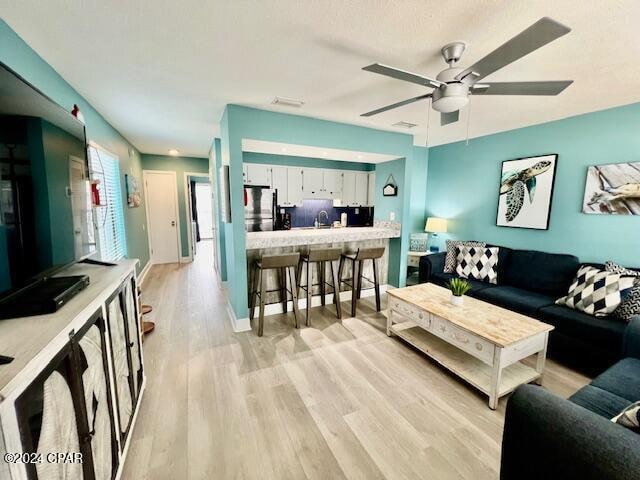 living room featuring ceiling fan, sink, and light wood-type flooring