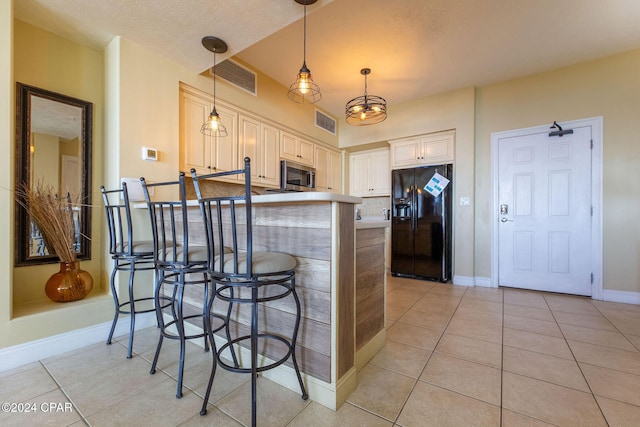 kitchen featuring decorative light fixtures, a breakfast bar area, light tile patterned floors, black fridge, and cream cabinetry