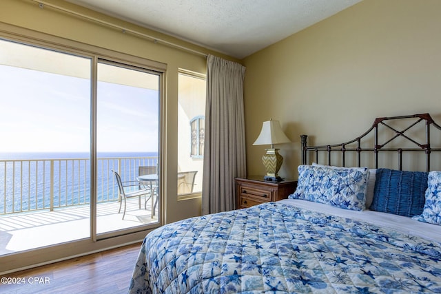 bedroom featuring a water view, hardwood / wood-style flooring, a textured ceiling, and access to outside