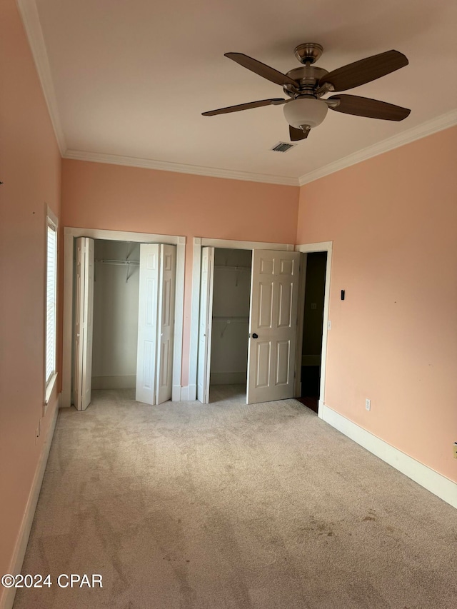 unfurnished bedroom featuring carpet flooring, two closets, and ornamental molding