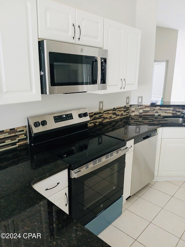 kitchen with white cabinetry, stainless steel appliances, dark stone counters, and light tile patterned floors