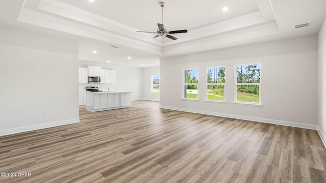 unfurnished living room featuring a raised ceiling, ornamental molding, ceiling fan, and light hardwood / wood-style flooring