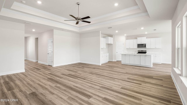 unfurnished living room featuring crown molding, a tray ceiling, ceiling fan, and light wood-type flooring