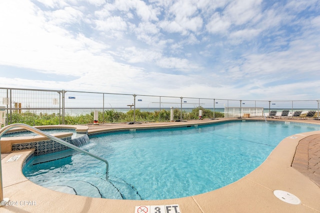 view of swimming pool with pool water feature and a hot tub